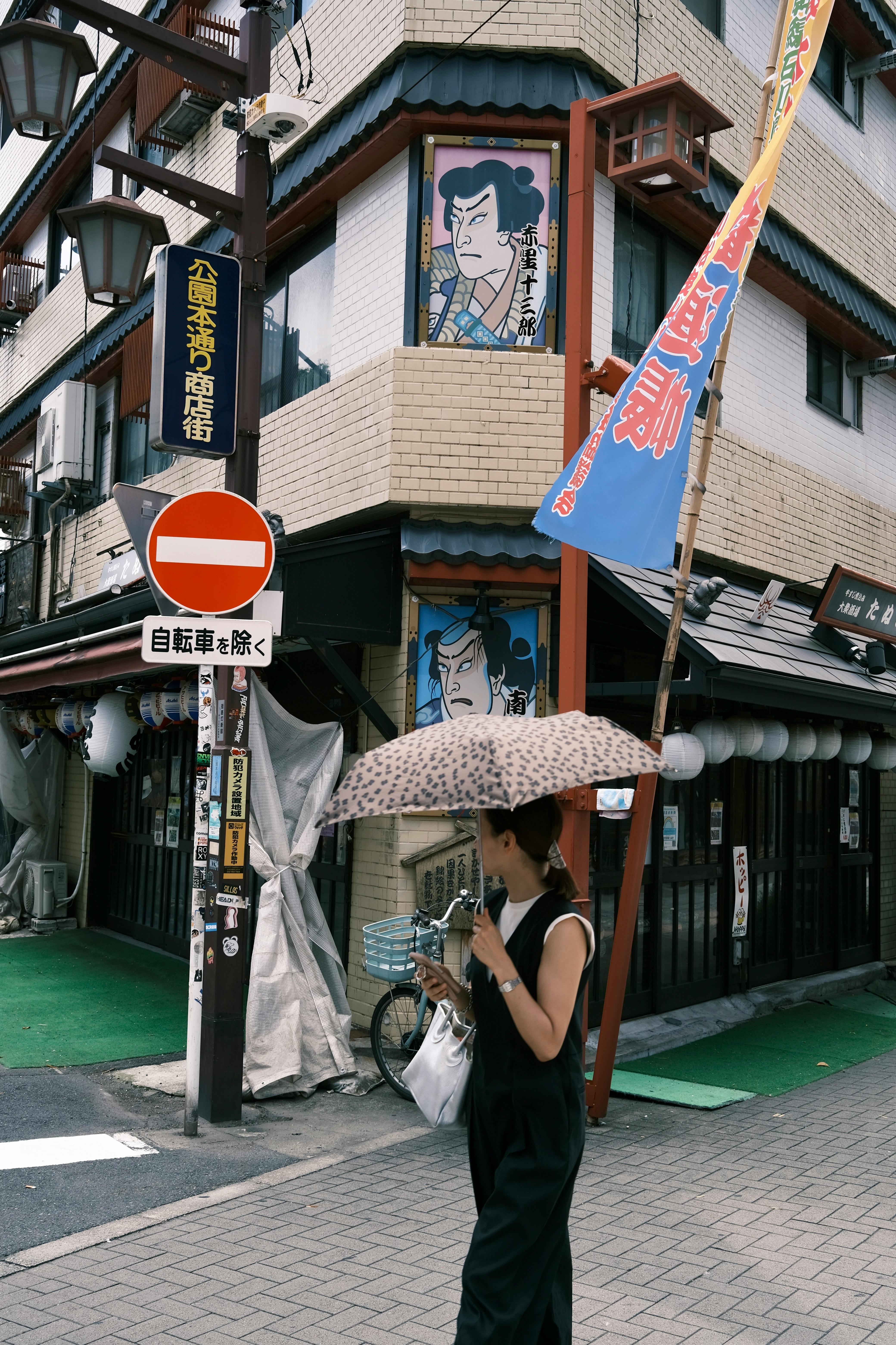 A woman with an umbrella walks past traditional shops in Taito City, Tokyo, Japan.