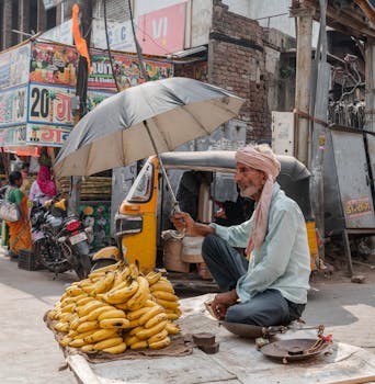 A street vendor in Mathura, India sells bananas under a shade umbrella on a busy street.