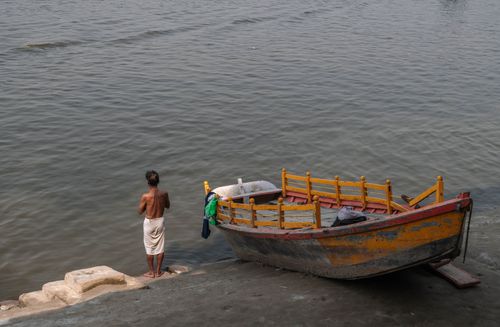 Free A man stands by a riverbank near a vibrant painted boat in Mathura, India. Stock Photo