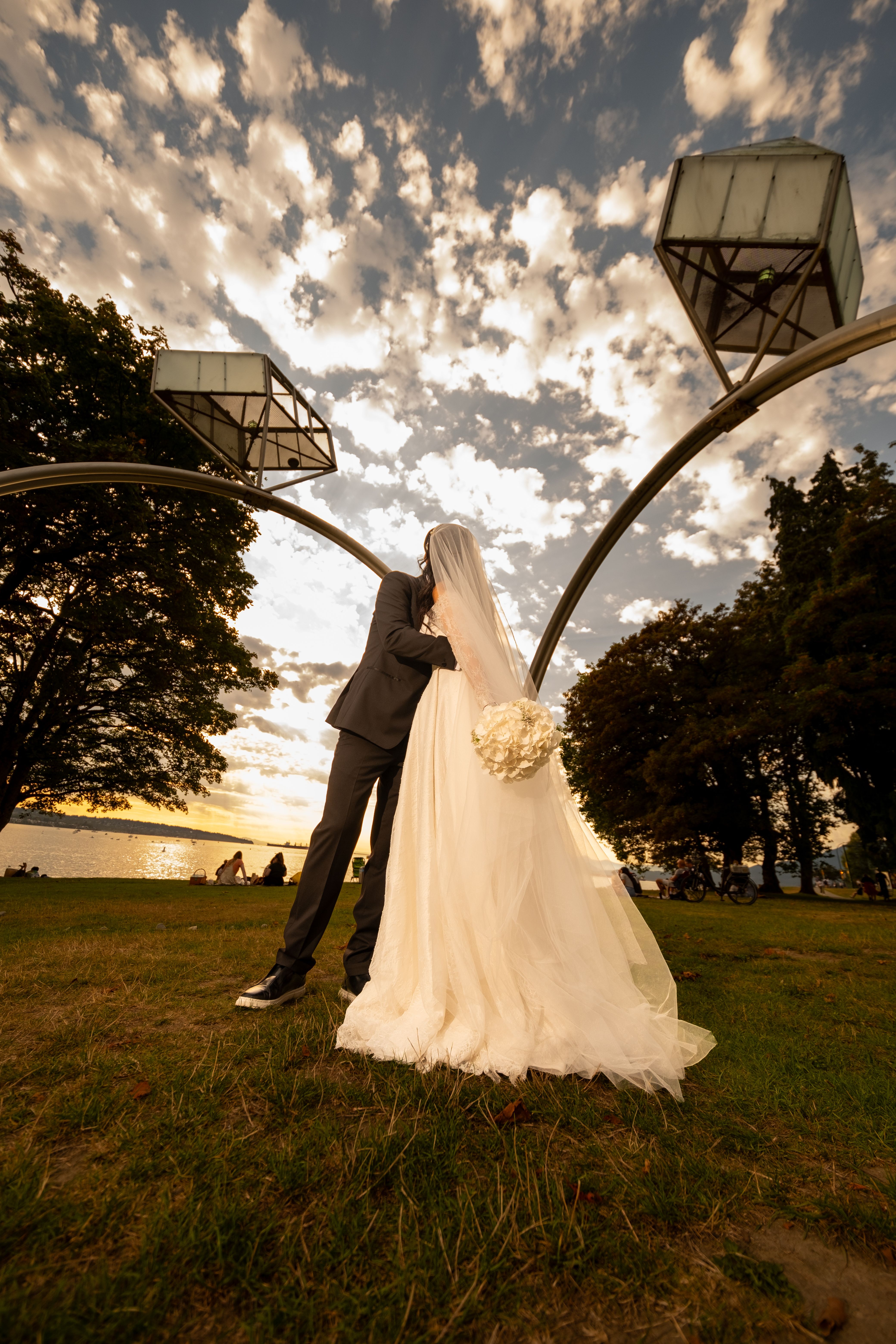 A couple kisses under a unique arch with a stunning sunset backdrop.