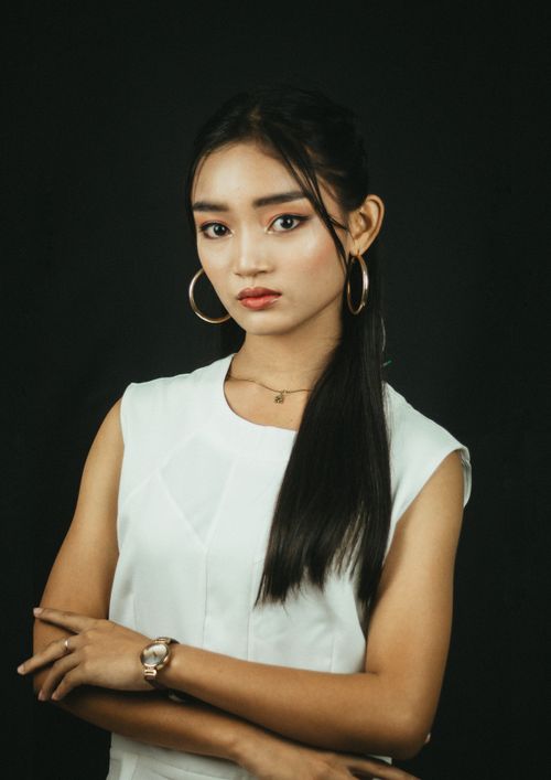 Free Striking portrait of a young woman wearing hoop earrings and white top against a dark background. Stock Photo