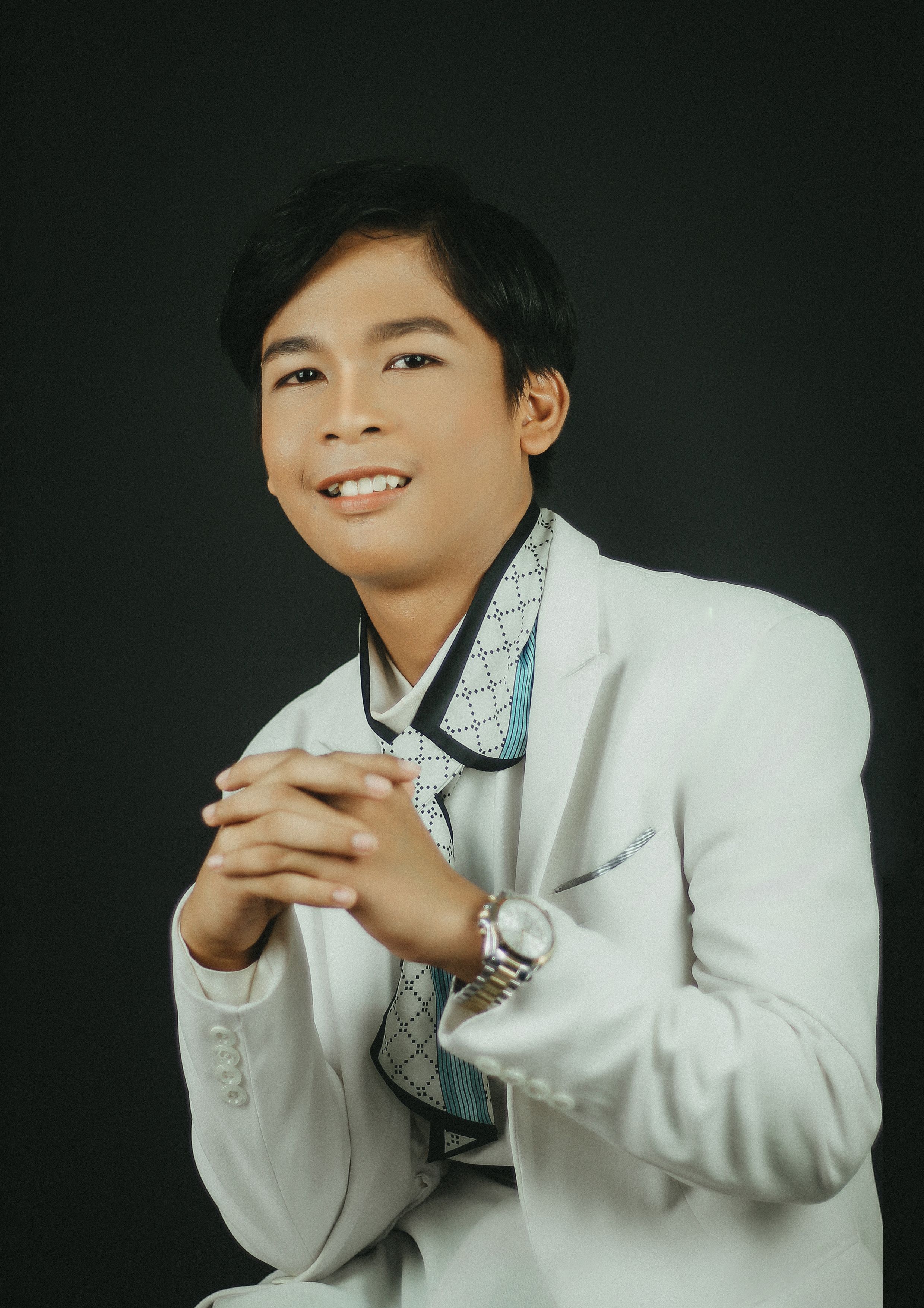 Portrait of a young man in a white suit with a black background, smiling and confident.
