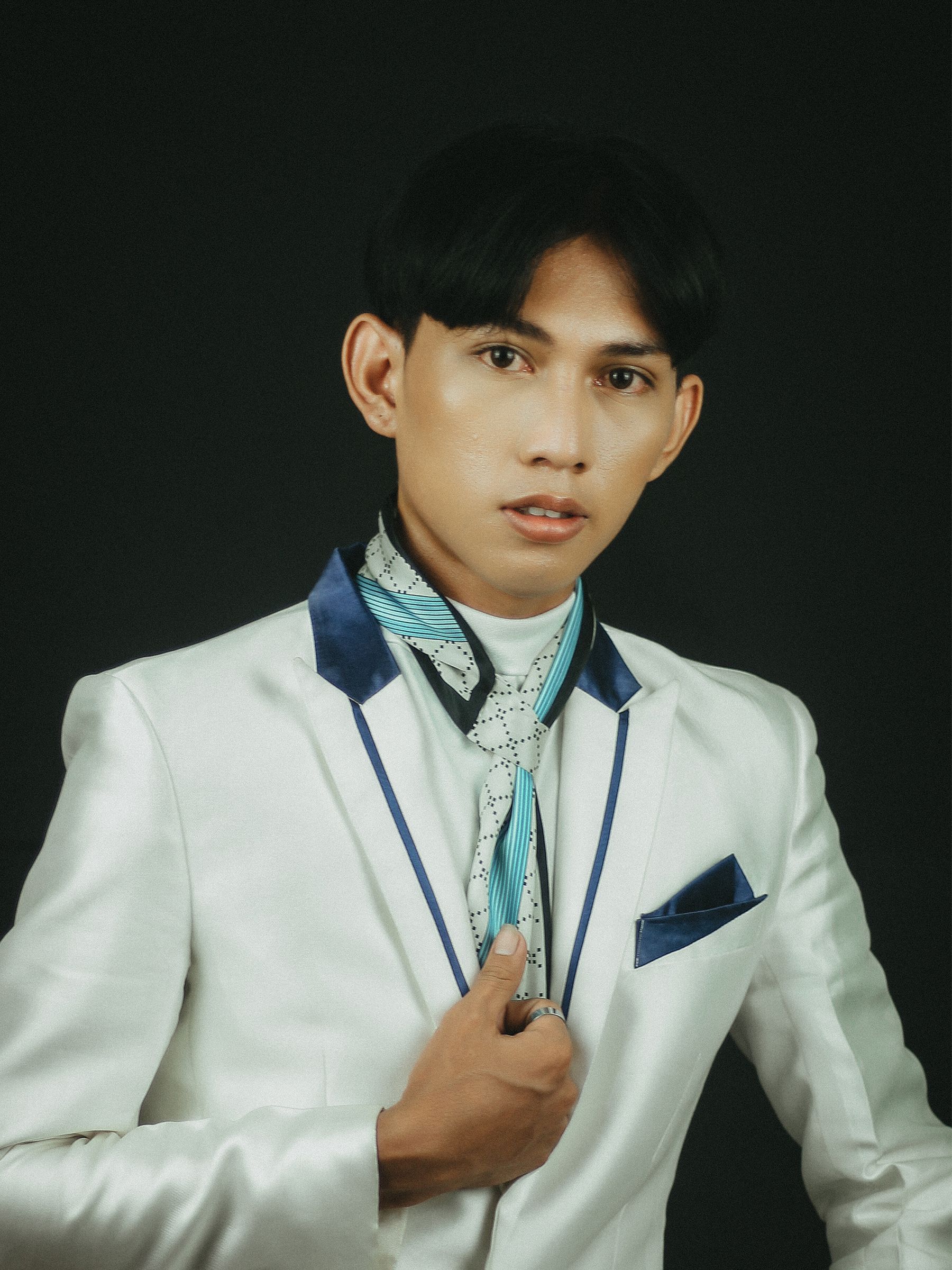 Stylish young man in a white suit posing confidently against a dark background.