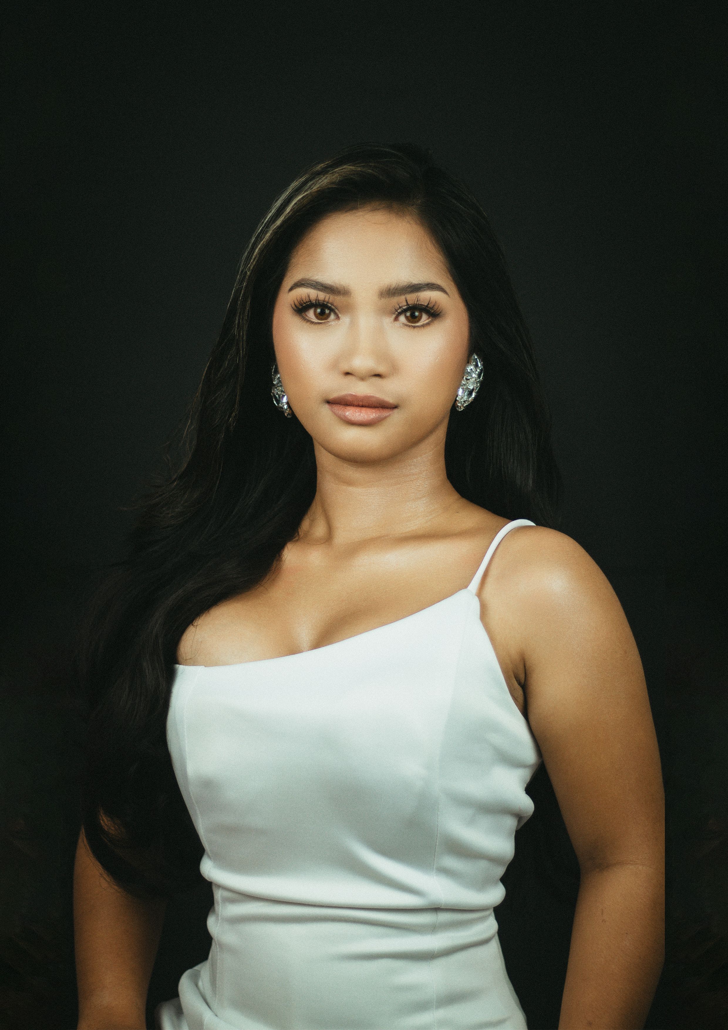 Beautiful woman in a white dress posing against dark background.