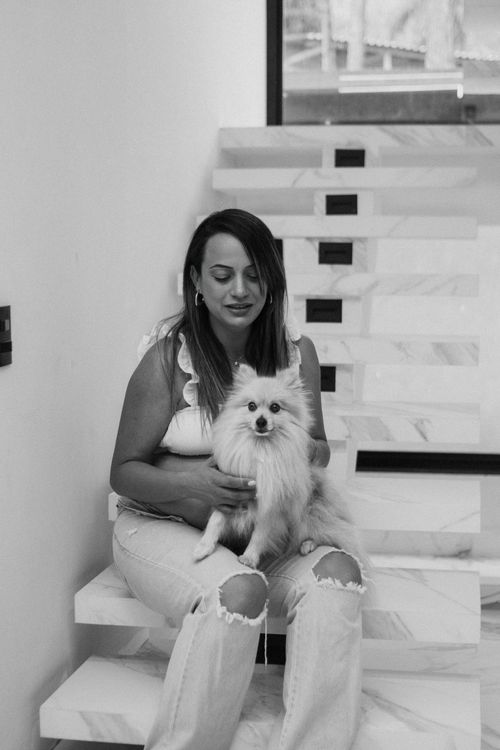 Free A woman sitting on marble stairs holding a fluffy Pomeranian indoors. Stock Photo