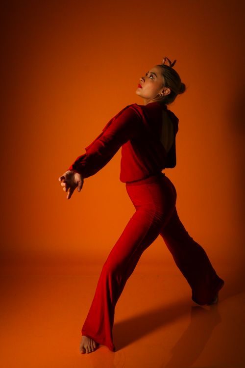 Free A dancer striking a powerful pose in a vibrant red outfit on an orange backdrop, capturing movement and grace. Stock Photo
