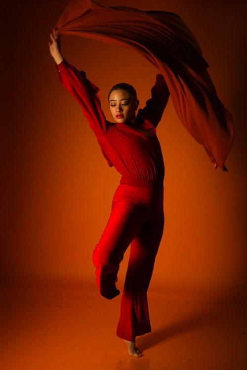Free A dancer in a striking red outfit performs a dynamic pose against an orange backdrop. Stock Photo