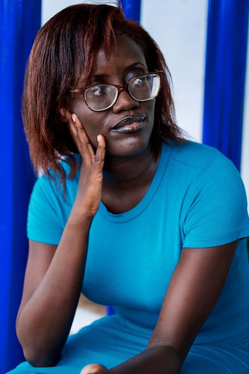Free A woman in a blue shirt sits thoughtfully, wearing glasses and resting on her hand. Stock Photo