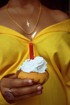 A close-up of a woman in yellow holding a cupcake with a lit red candle.
