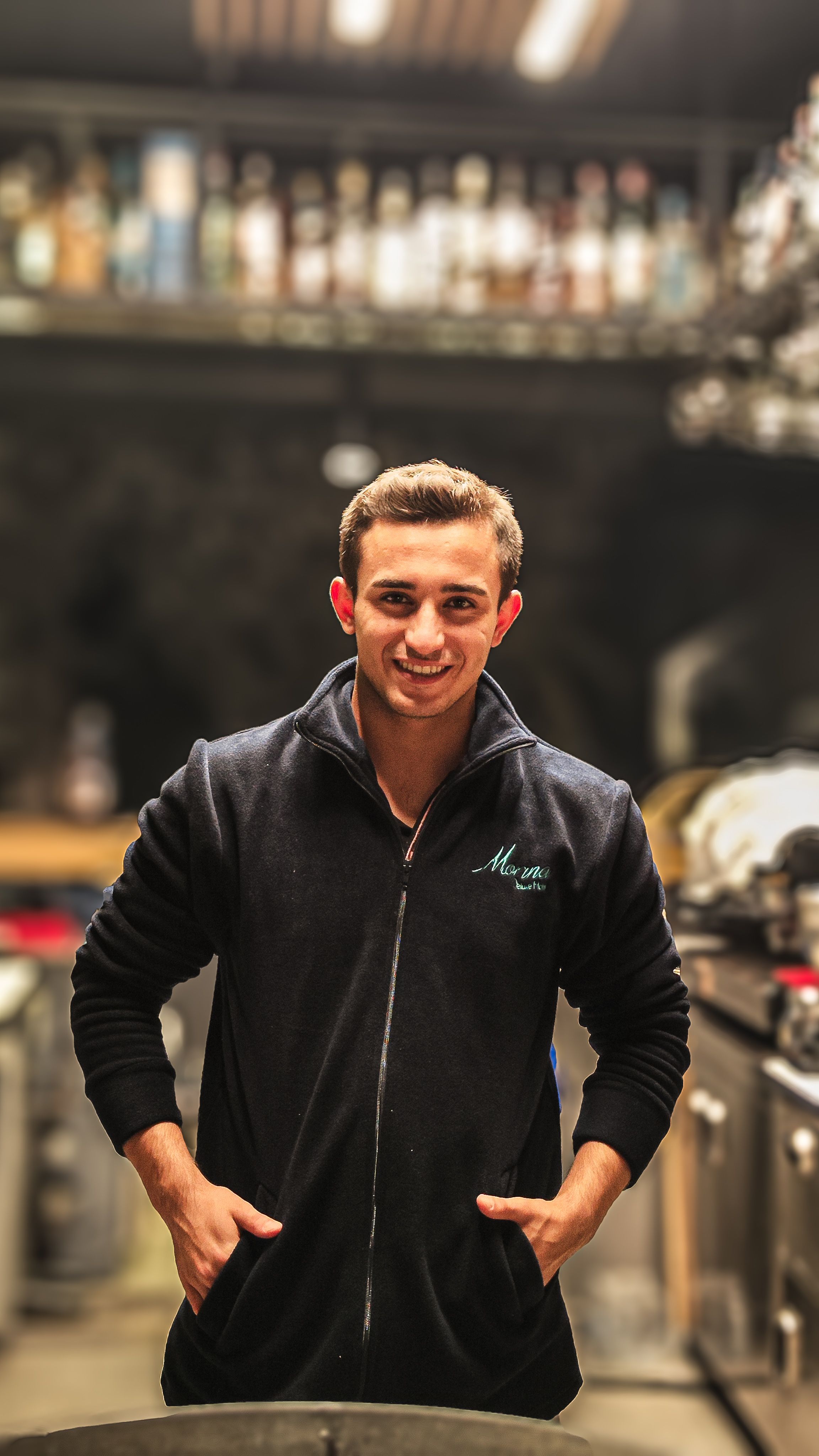 A smiling chef standing confidently in a modern restaurant kitchen.