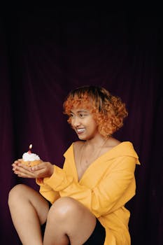 Young woman celebrating her birthday with a candlelit cupcake, smiling joyfully.