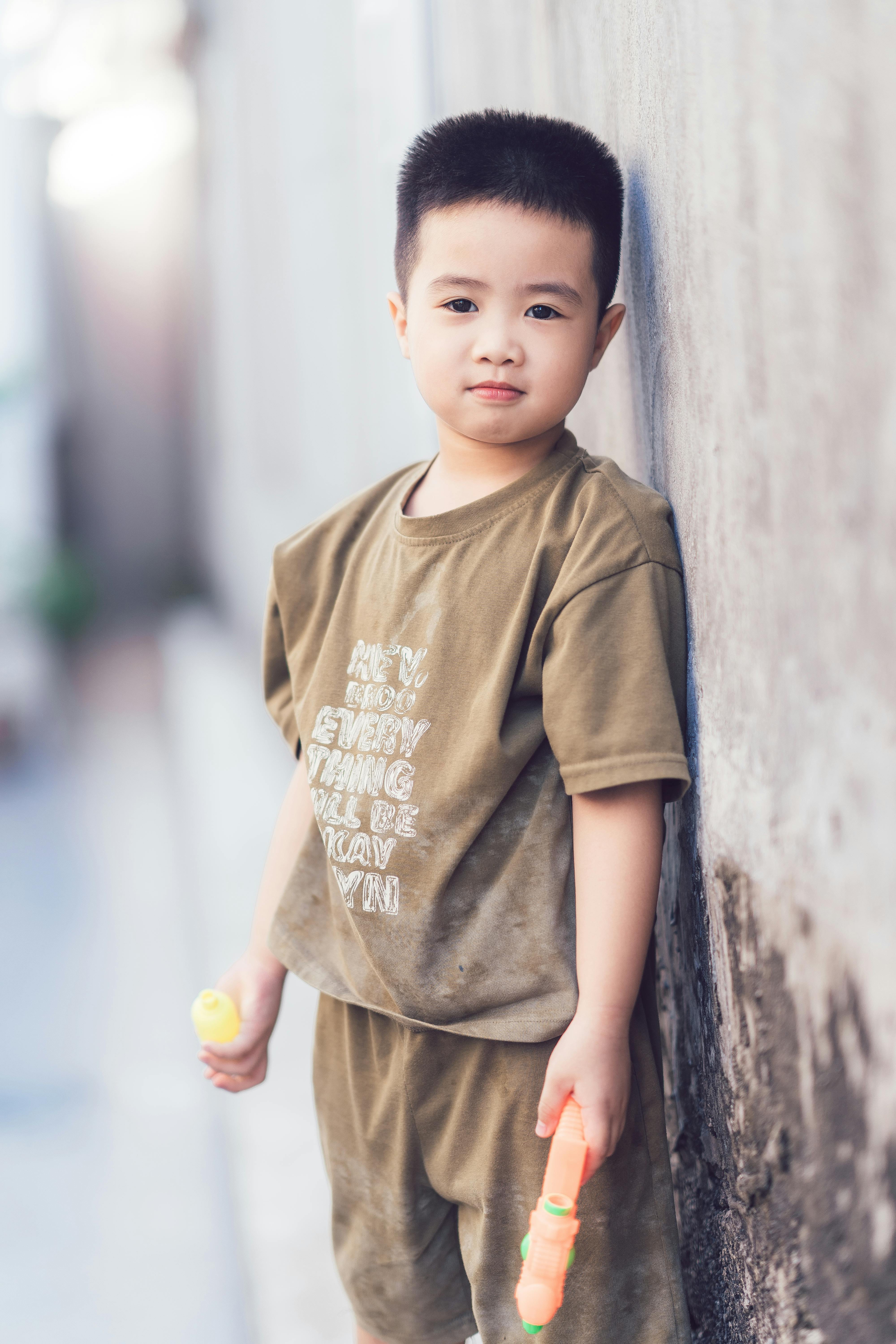 Child standing in an alley with water gun, relaxed expression, casual clothing.