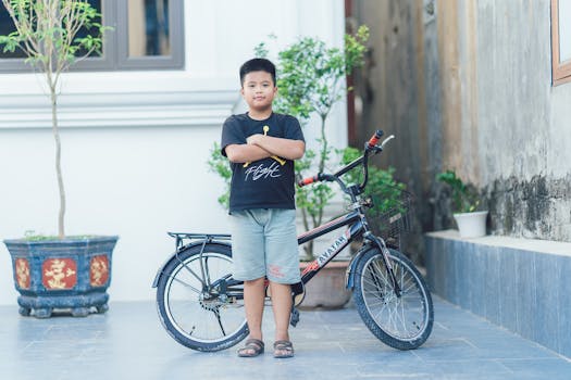 A young boy stands proudly beside his bicycle in an urban setting. Reflects confidence.