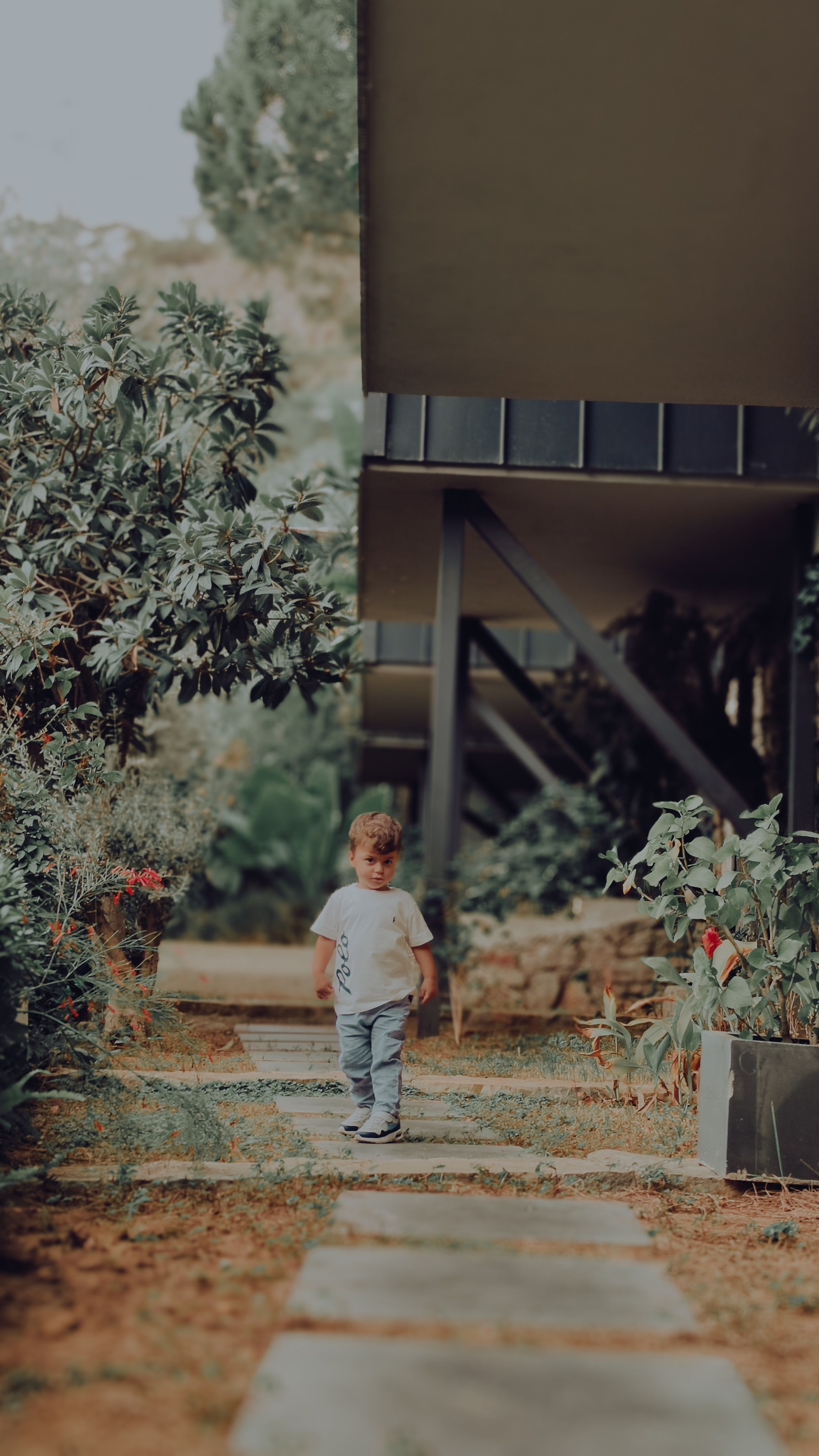 A young child in a garden setting beside a modern building.