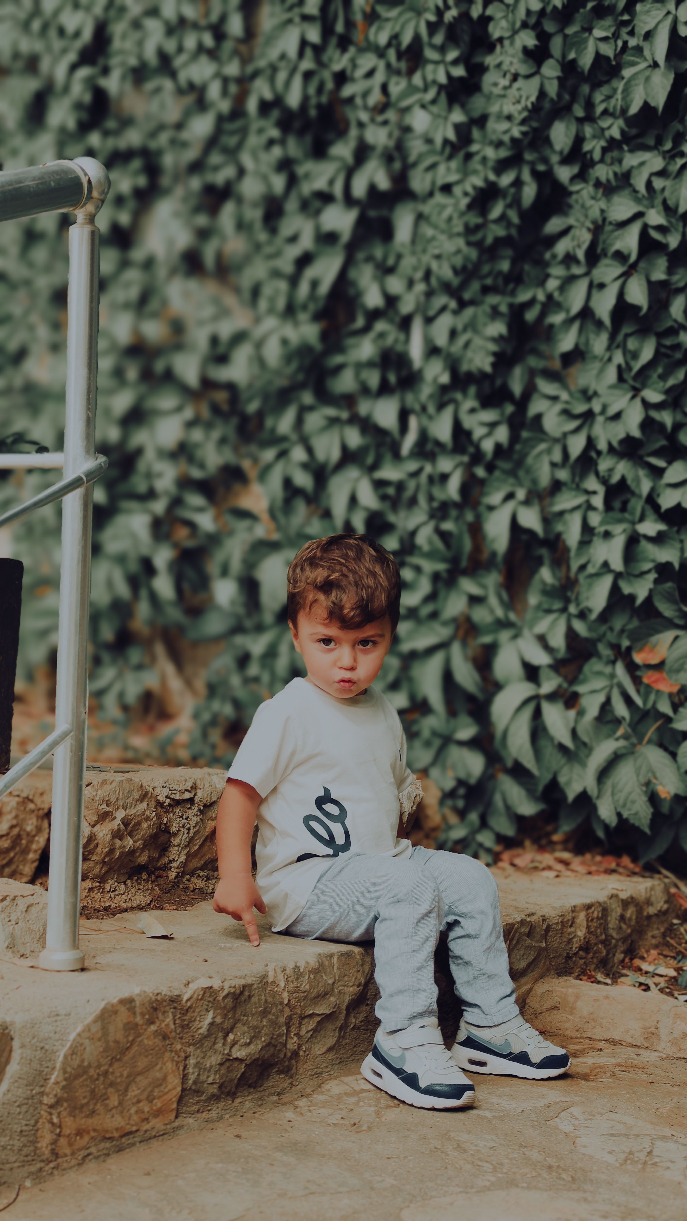 Niño Sentado Al Aire Libre Junto A Una Pared Frondosa · Foto de stock ...