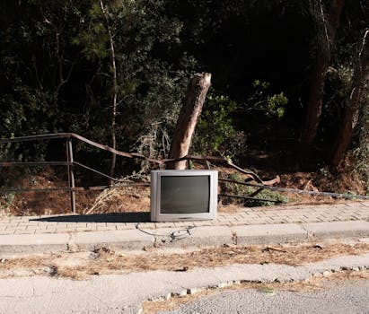 An abandoned tube television on a sidewalk surrounded by nature in Izmir, Türkiye.