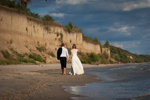 Bride and groom walking hand-in-hand by cliffs on Ukrainian beach.
