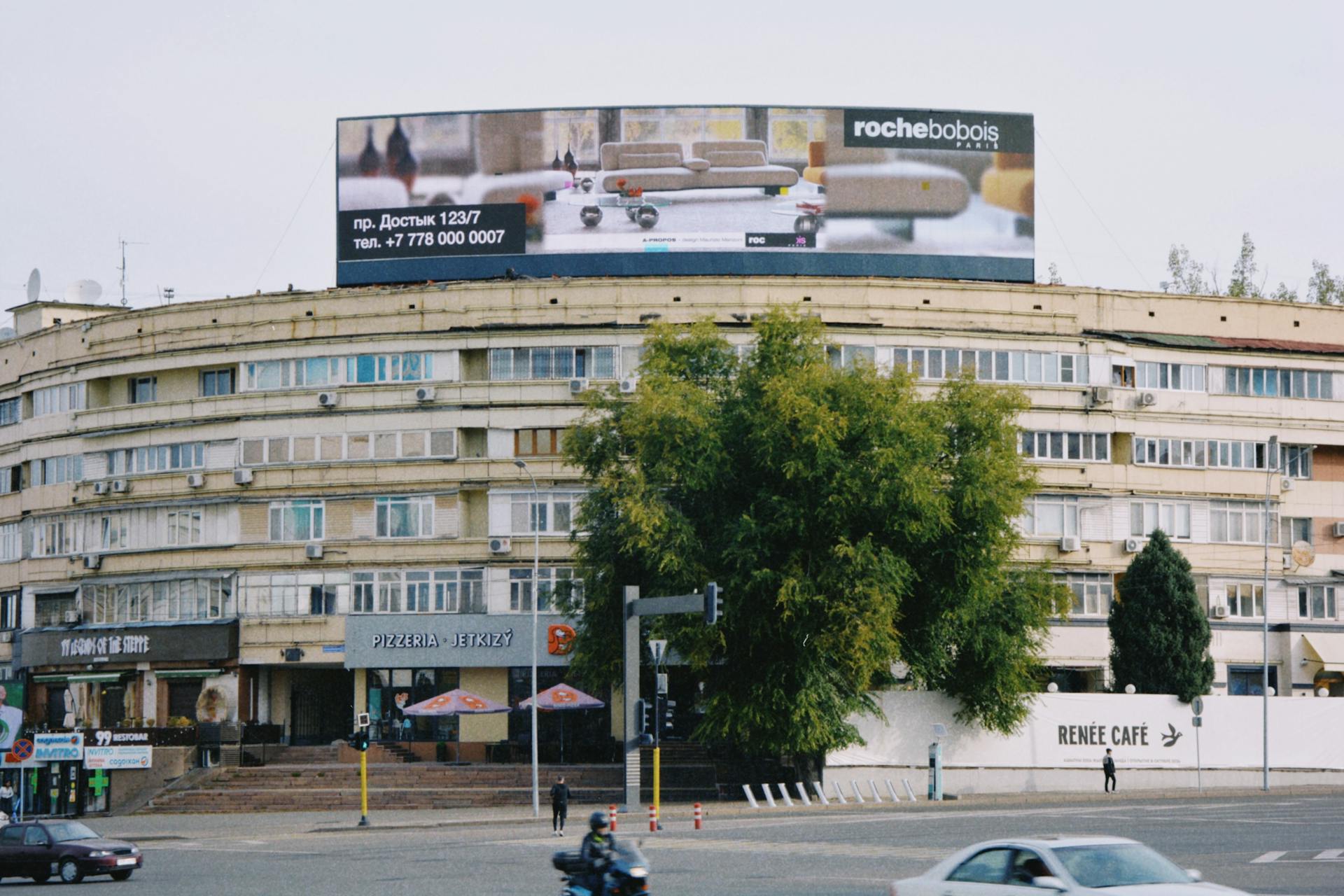 View of a round building with a prominent billboard in Almaty, Kazakhstan.