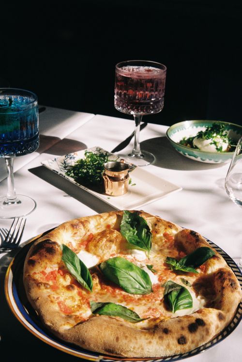 Free Fresh Italian pizza with basil on a table with drinks and side dishes. Stock Photo