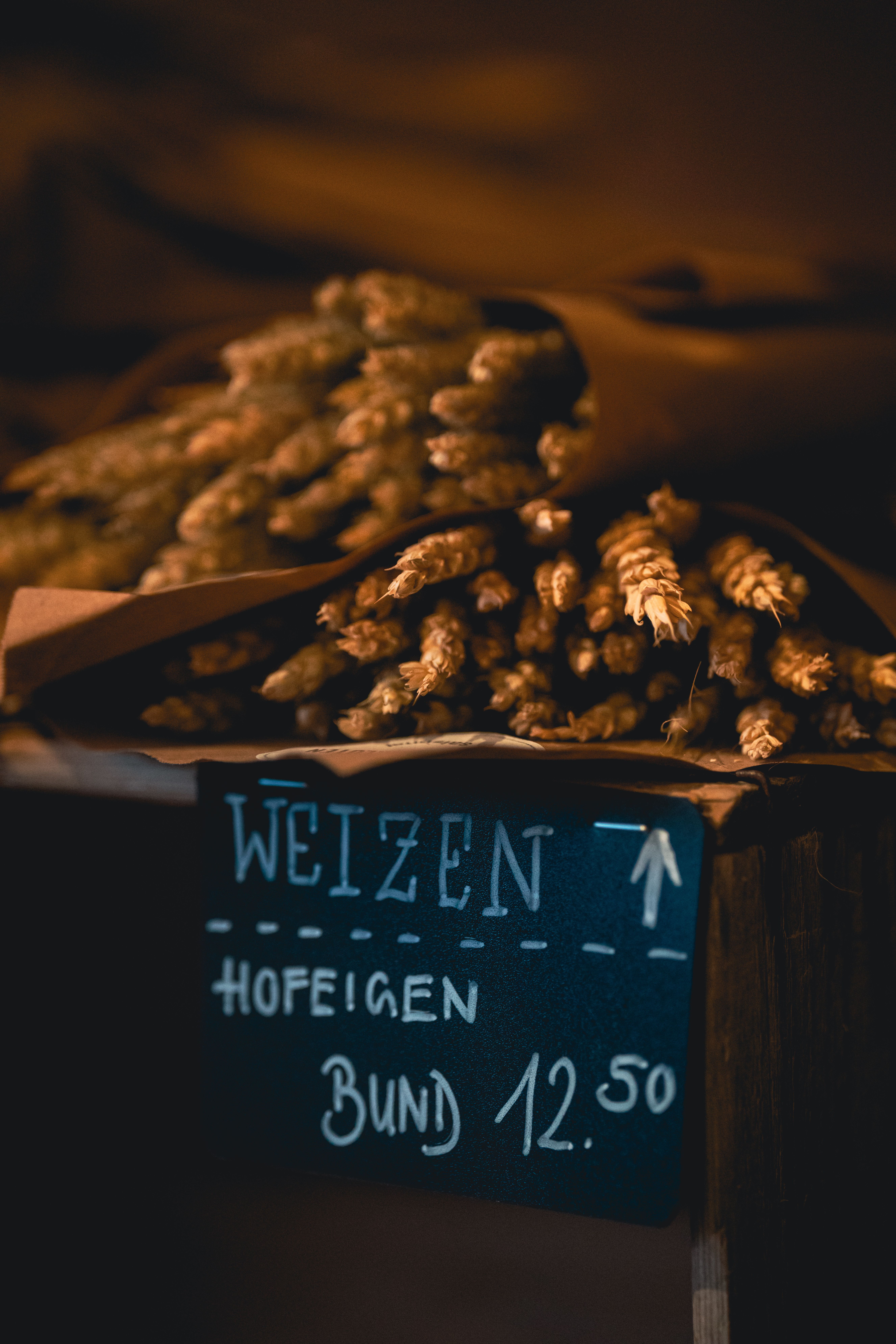 Dark and warm-toned image of wheat bundles with a hand-written price sign at a cozy market setting.