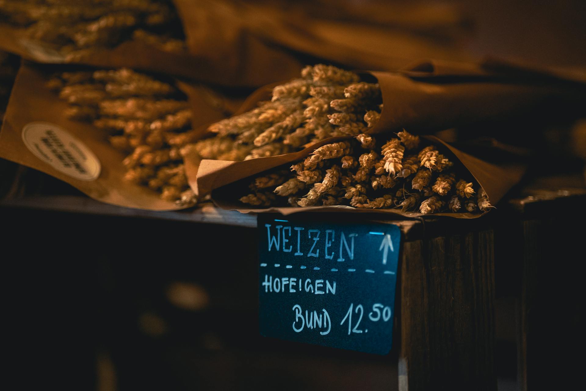 A rustic bundle of Weizen wheat on display in a market setting, prices marked in German.