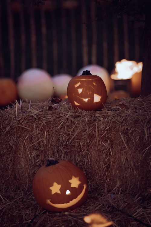 Free Two carved pumpkins glowing with candlelight on hay bales, creating a spooky Halloween ambiance. Stock Photo
