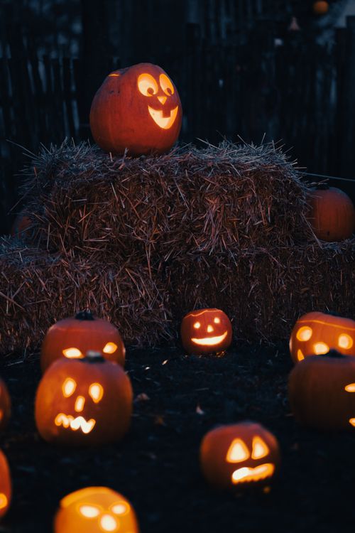 Free Spooky jack-o'-lantern pumpkins glowing on hay bales, perfect for Halloween ambiance. Stock Photo