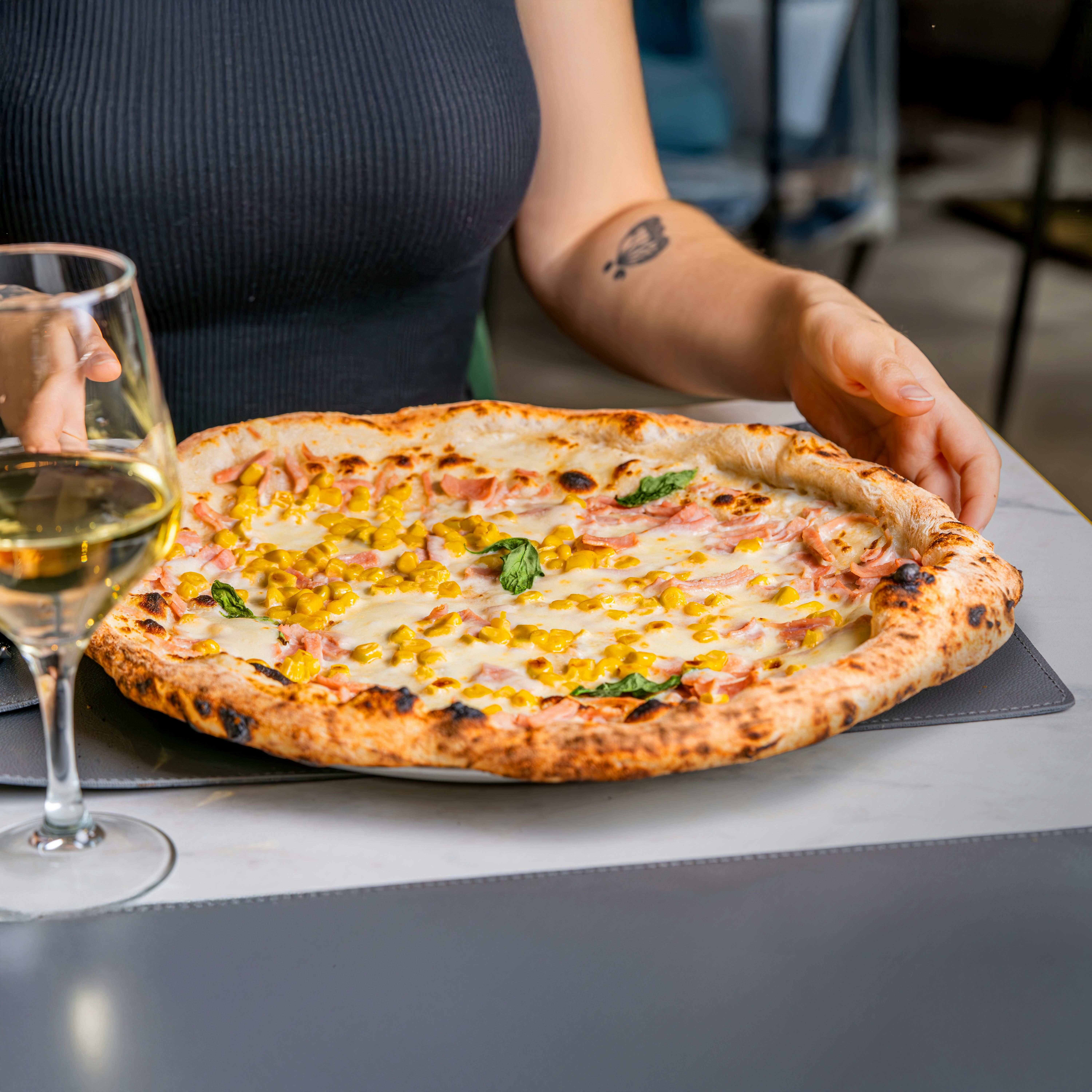 Wood-fired Margherita pizza with toppings and wine, captured indoors.