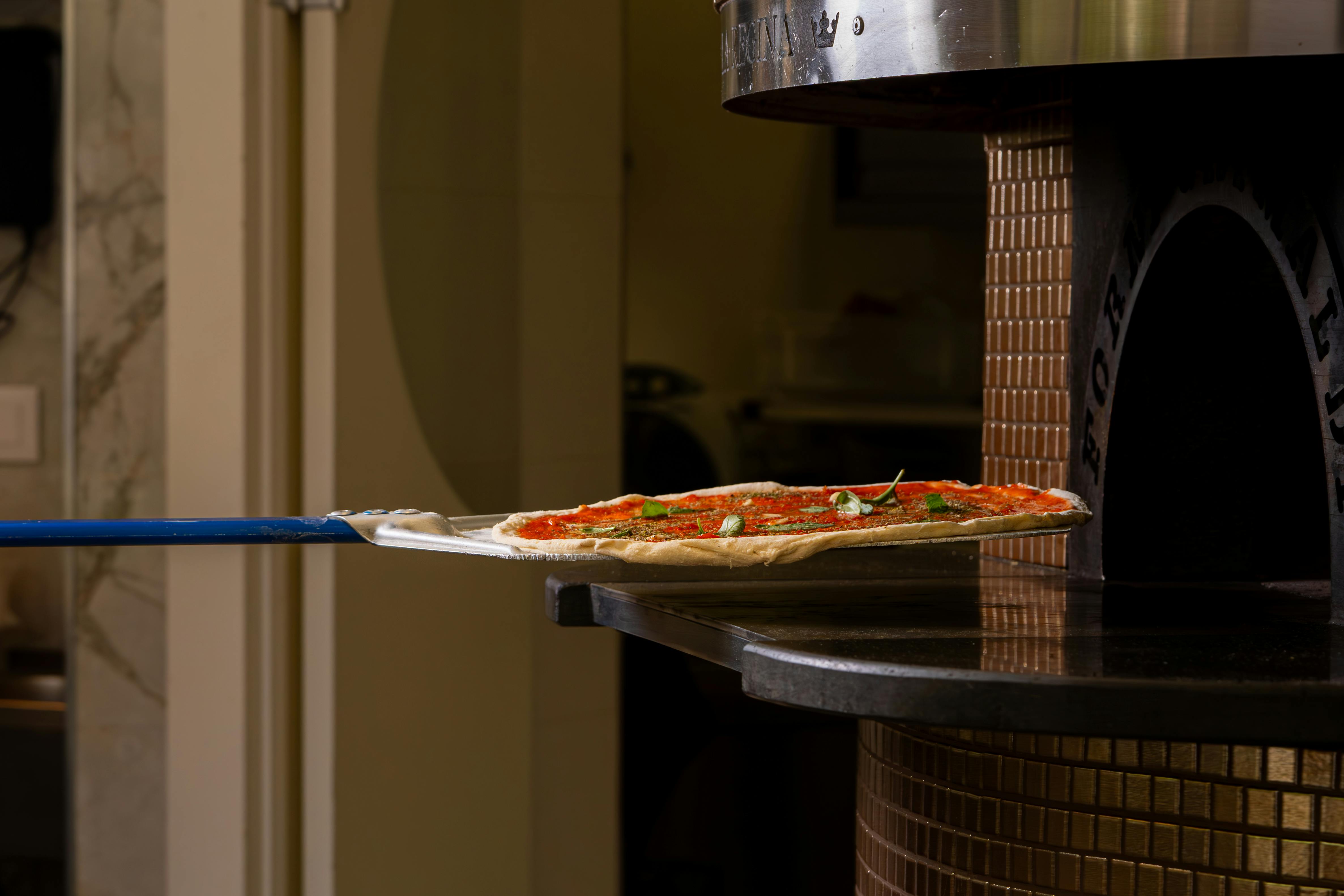 A classic pizza with fresh ingredients entering a wood fired oven for baking.