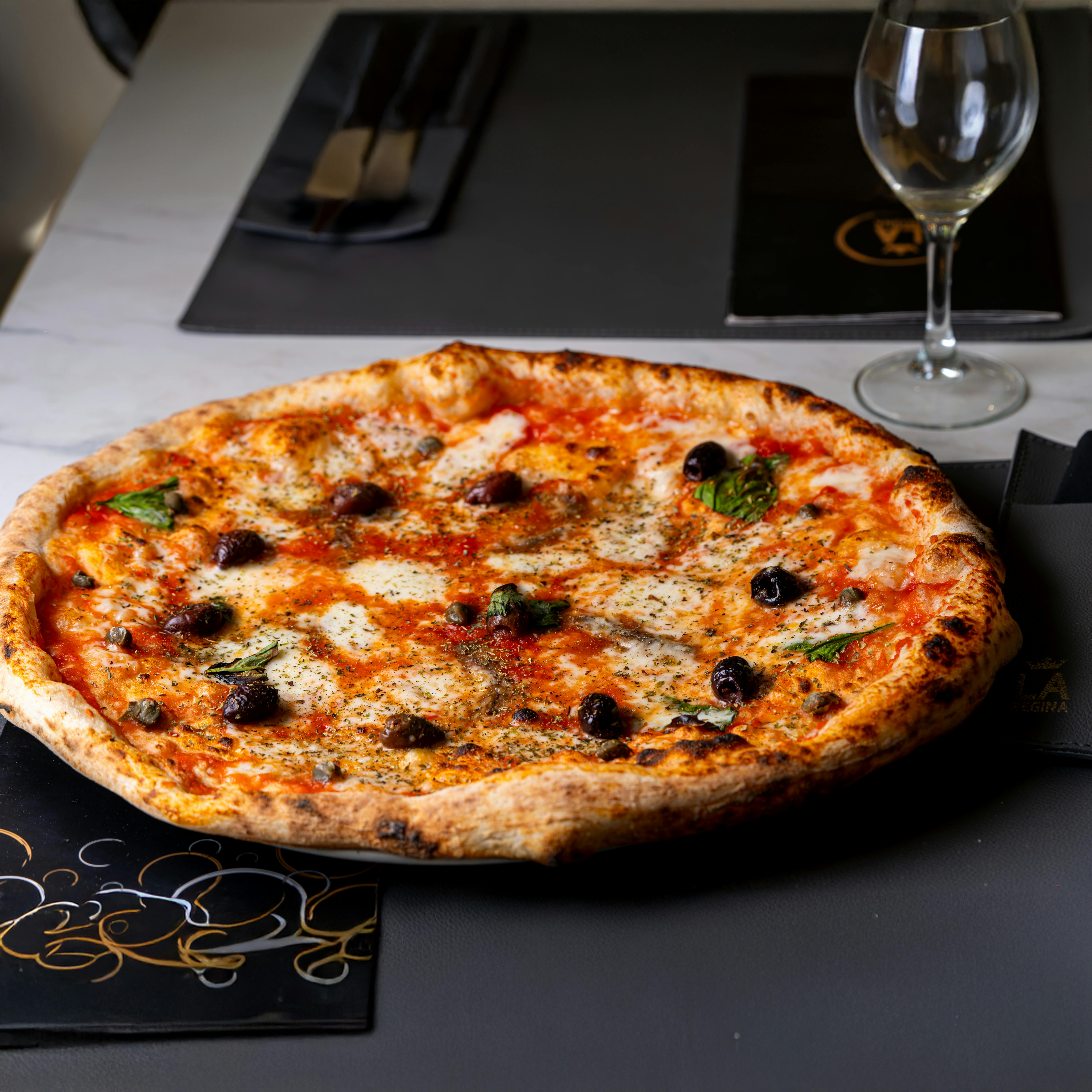 Wood-fired Margherita pizza with olives, served on a restaurant table with elegant tableware.
