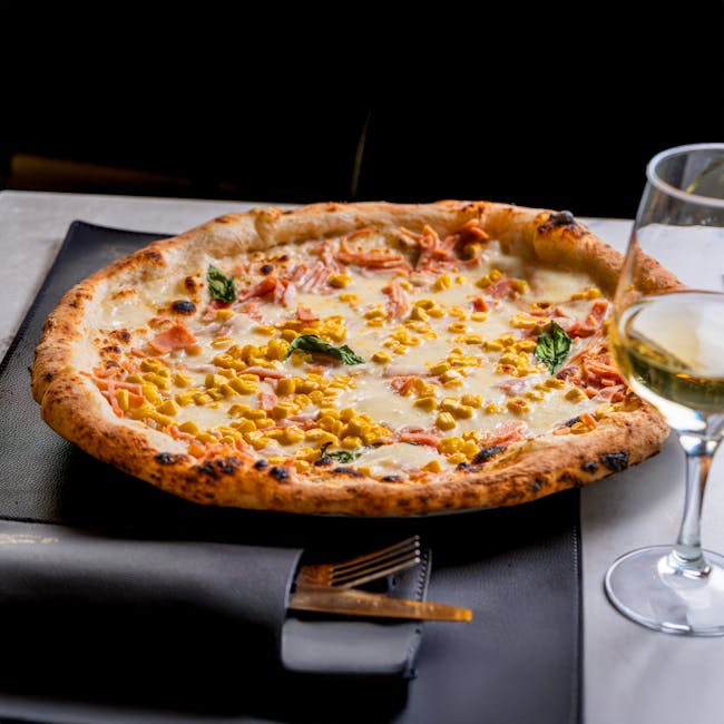 Authentic Italian pizza topped with corn, basil, and cheese, served with a glass of wine.