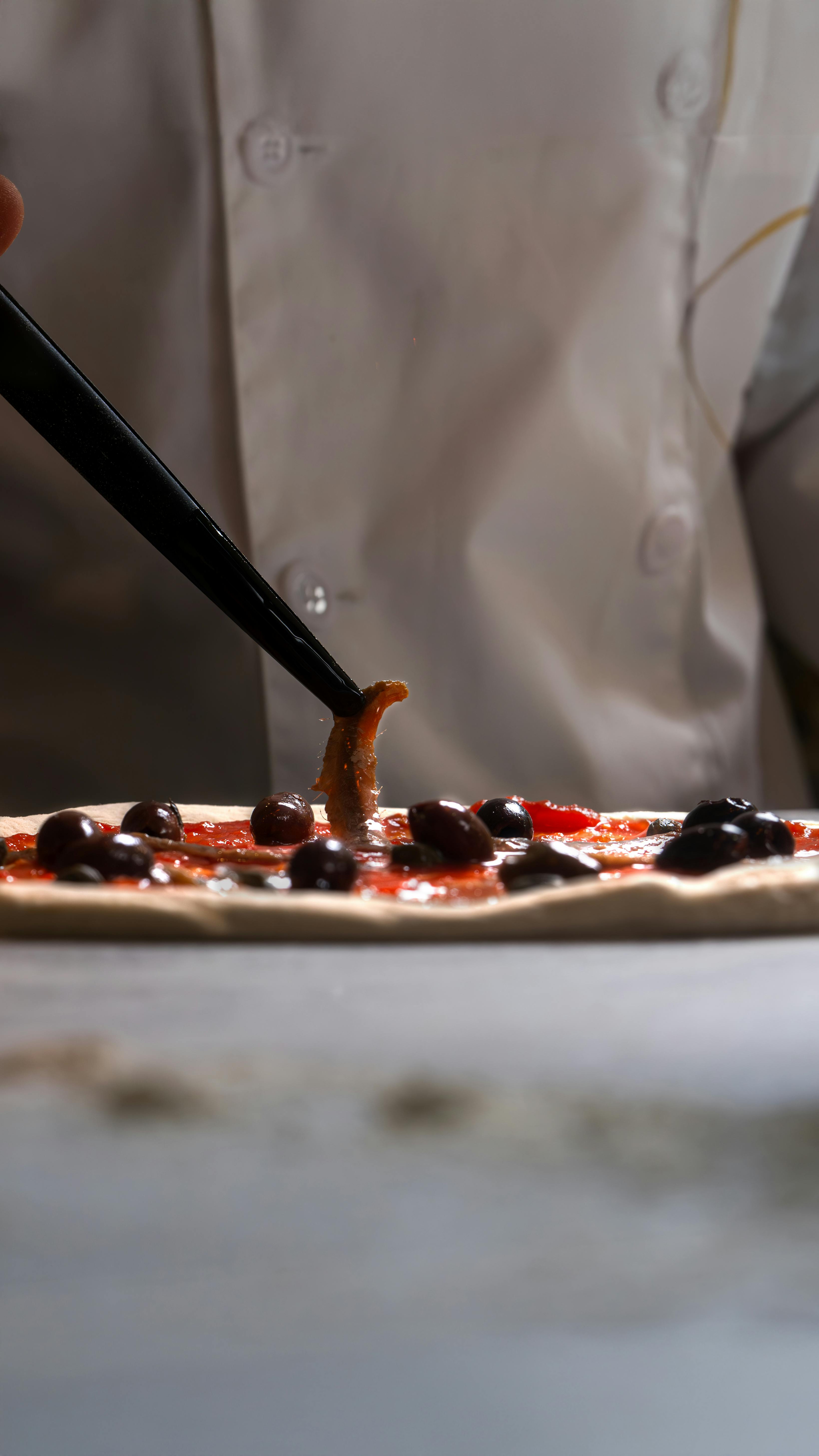 Close-up of a chef adding olives to a pizza with precision in a kitchen.