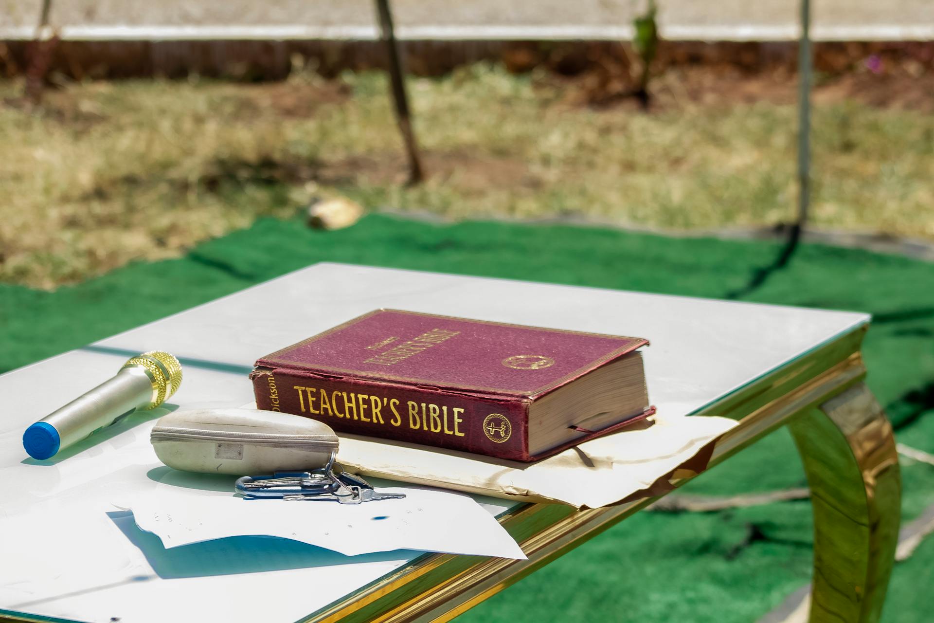 Outdoor table setup with a Teacher's Bible and microphone. Ideal for educational or religious themes.