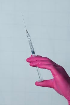 A syringe held by a hand in pink gloves against a light background.