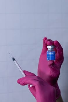 A medical professional holding a vaccine vial and syringe with pink gloves.