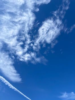 Clear blue sky in Dubai with wispy white clouds and a vapor trail, offering serene visuals.