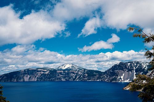 Free Breathtaking view of Crater Lake surrounded by snow-capped mountains under a vibrant blue sky with clouds. Stock Photo