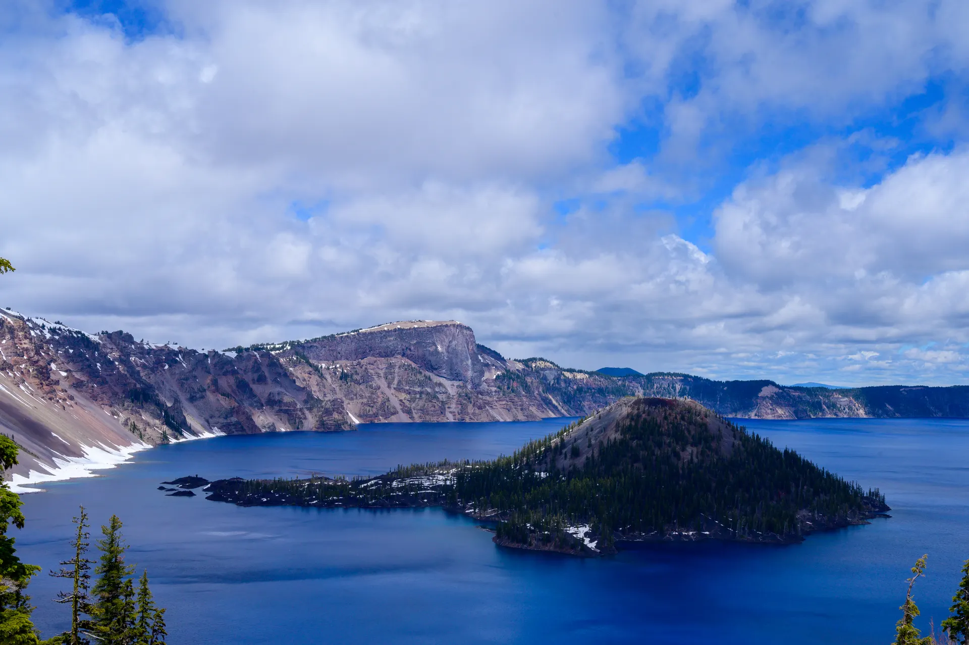 View of Crater Lake with Wizard Island surrounded by clouds and conifer trees. View of Crater Lake with Wizard Island surrounded by clouds and conifer trees.