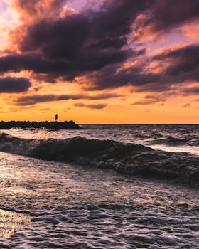 剪影中的人物站在岩石海岸上，头顶是海浪与戏剧性的日落天空