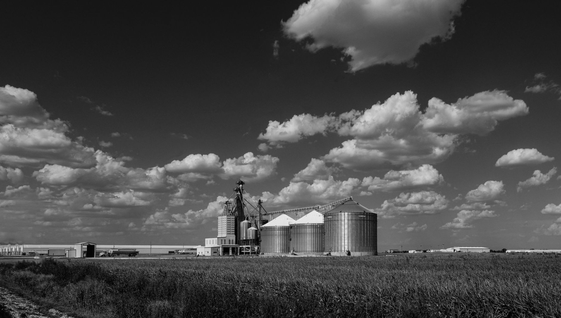 Black and white photo of silos under a cloudy sky in a rural landscape.
