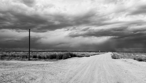 Free Black and white photo of a desolate rural road under dramatic cloudy skies. Stock Photo