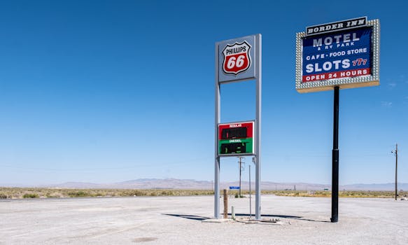 Desolate desert gas station with Route 66 and motel signs under a clear blue sky.