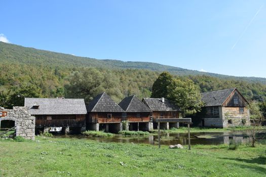 Charming old wooden mills by the Gacka River in Sinac, Croatia, under clear blue skies.