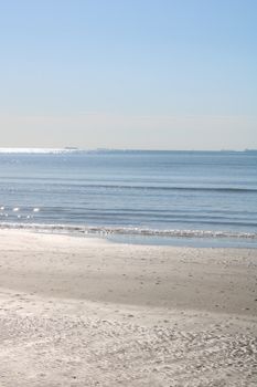 Peaceful beach scene capturing gentle ocean waves and shimmer on a clear day.