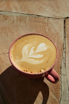 Aerial view of intricate latte art in a pink cup on a wooden surface.