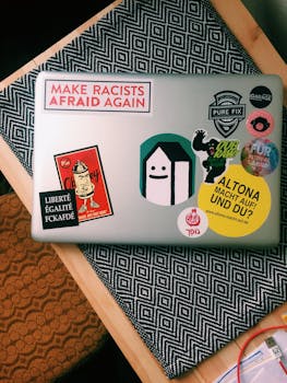 办公桌上放着一台笔记本电脑，上面贴着色彩缤纷的政治和艺术主题贴纸