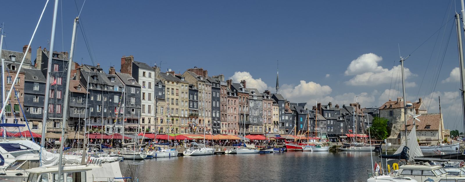 Explore the picturesque harbor of Honfleur, France, featuring vibrant traditional houses and sailing boats.