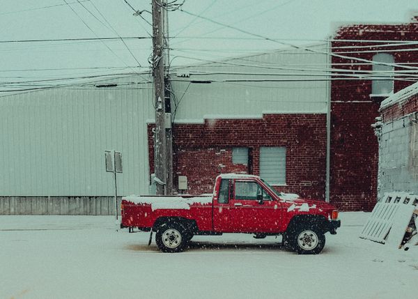 Red pickup truck parked in falling snow on a quiet street — photo by Zachariah Garrison on Pexels