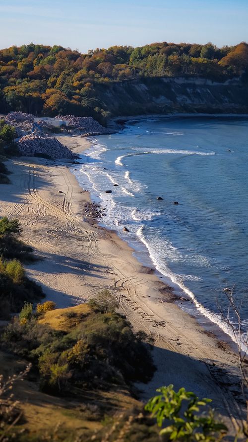 Free A picturesque beach with gentle waves and colorful autumn foliage, perfect for nature lovers. Stock Photo
