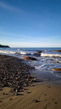Serene view of waves lapping against a pebble-covered beach under a clear blue sky.